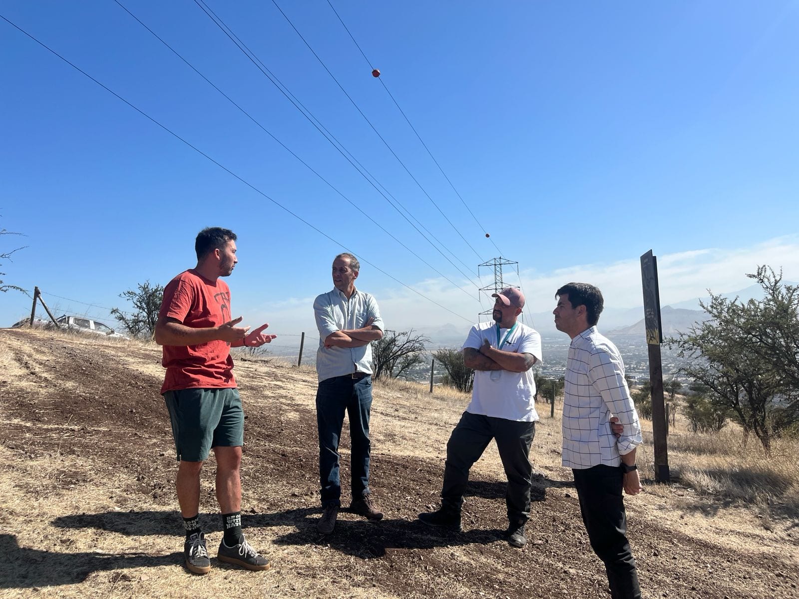Cuatro personas conversando en una ladera con la ciudad y la cordillera al fondo